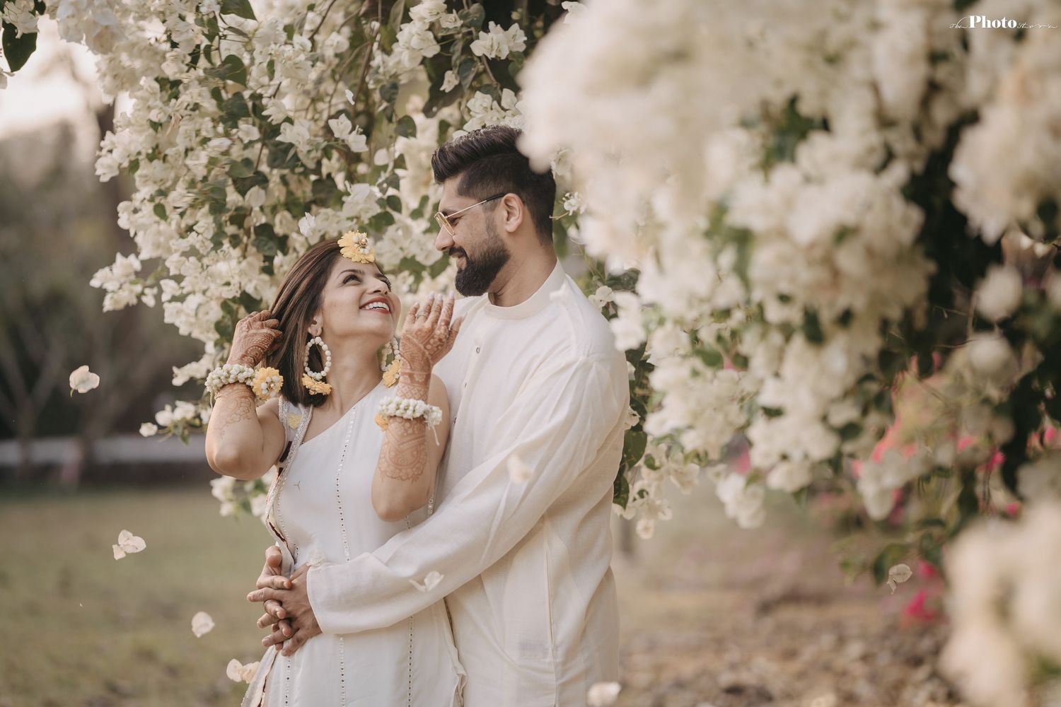 Couple shares intimate moment surrounded by delicate white spring blossoms in natural light.