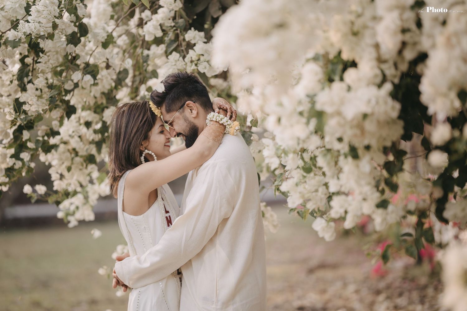 Elegant couple poses beneath flowering white cherry blossom branches in garden setting.