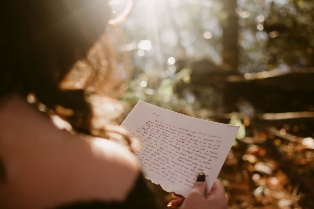 Handwritten letter being read in golden sunlit woods with bokeh lighting effects.