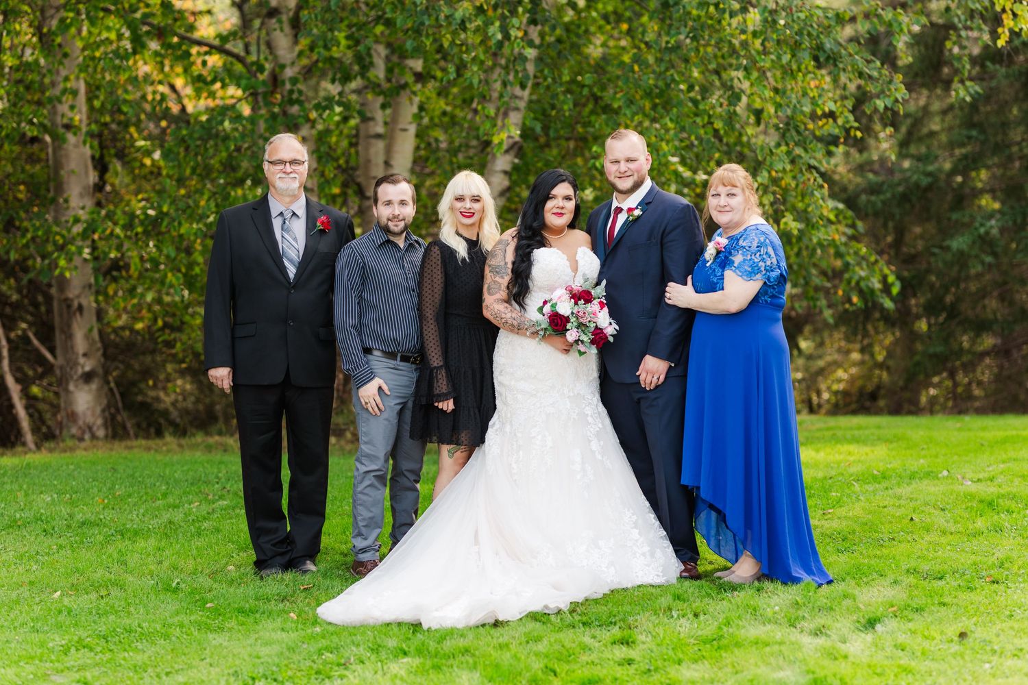 Wedding party members in navy and royal blue attire pose for formal photos on a lawn.