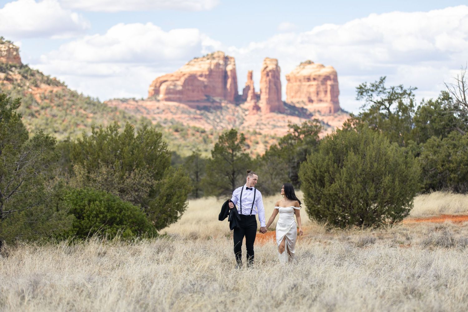 Wedding couple walking in field, Cathedral mountain Sedona, Arizona.
