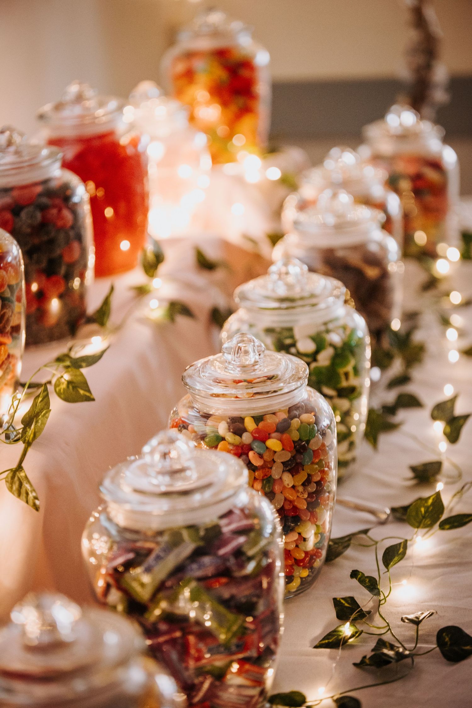 Decorative glass jars filled with colorful items arranged with fairy lights and greenery.