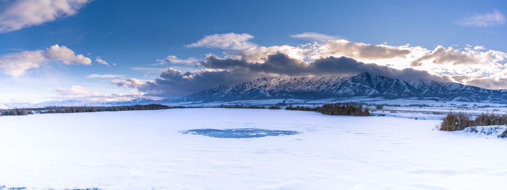 Snowy winter landscape with mountains and frozen lake under blue sky.