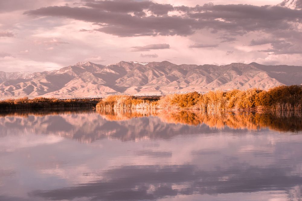 Mountain range reflected in calm lake water during golden hour.