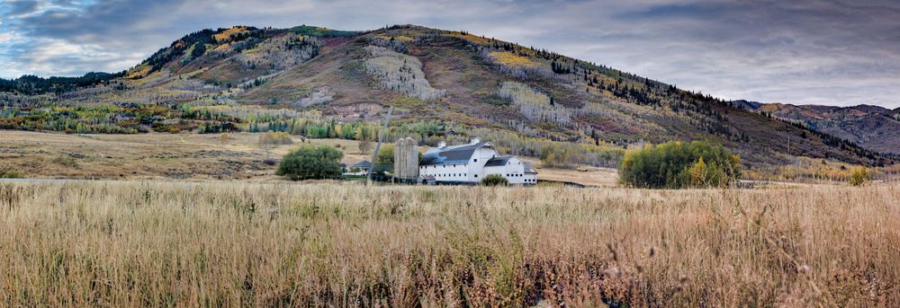 Panoramic view of white barn nestled in rolling hills with autumn colors.