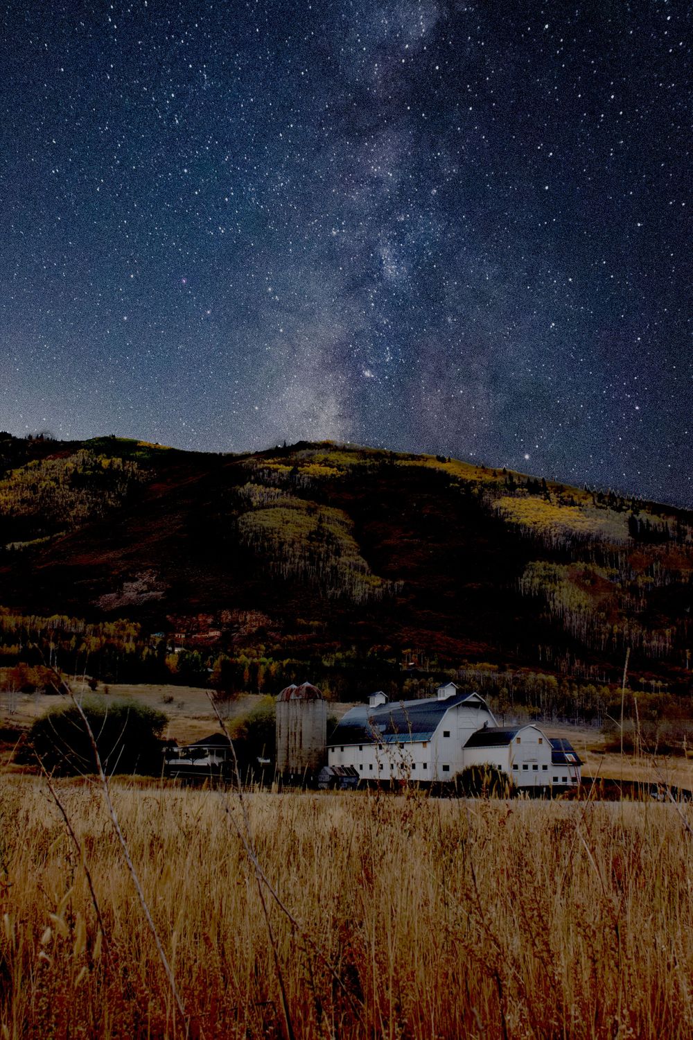 Rural barn under spectacular Milky Way night sky in mountain valley.