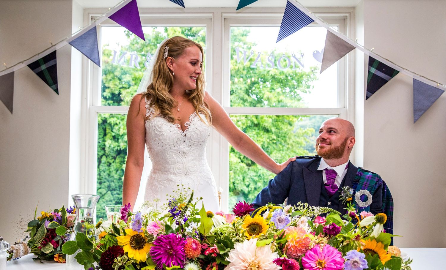 Colorful floral decorations and bunting adorn a bright wedding reception venue.