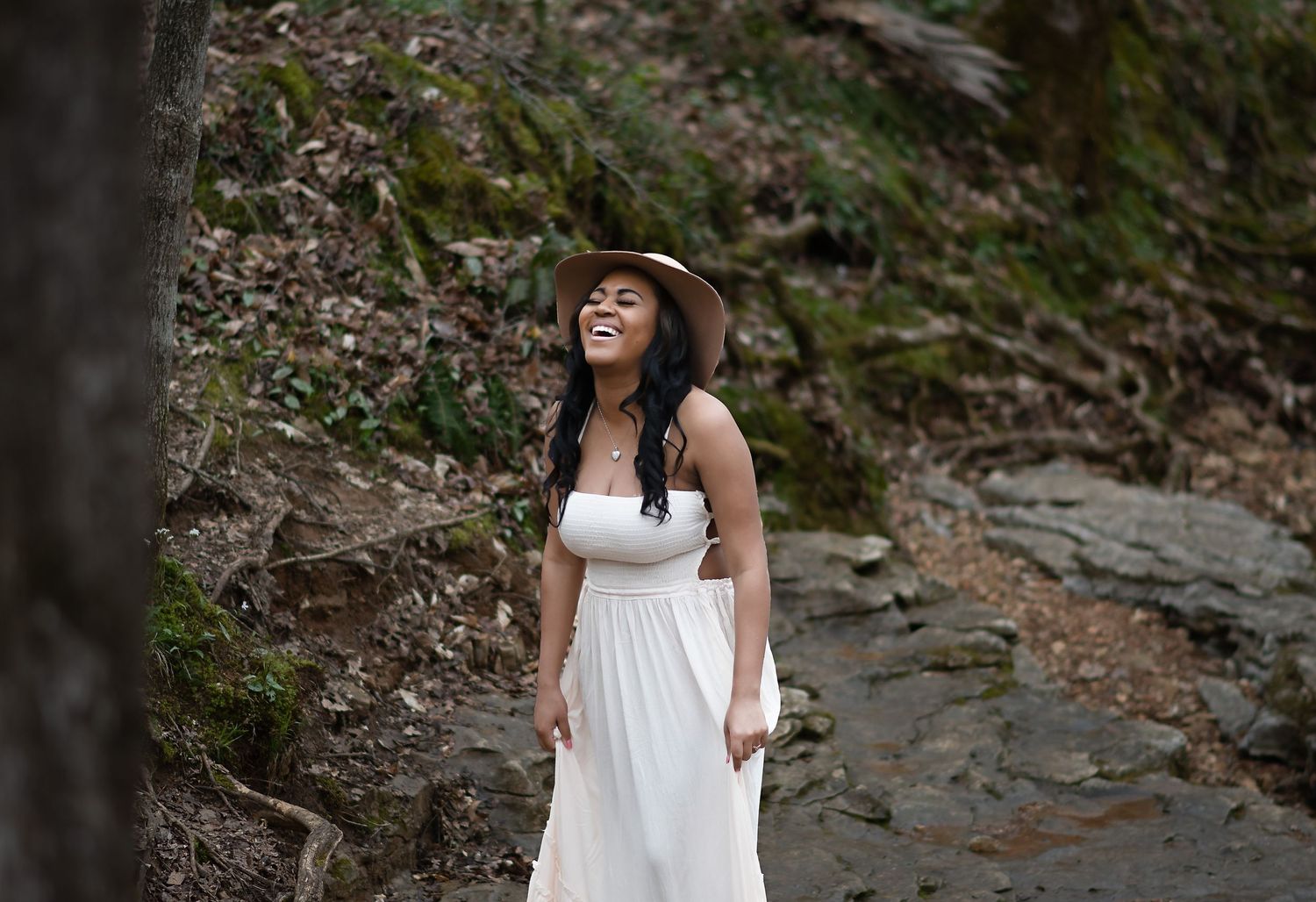 Woman in white dress posing serenely on rocky forest path.