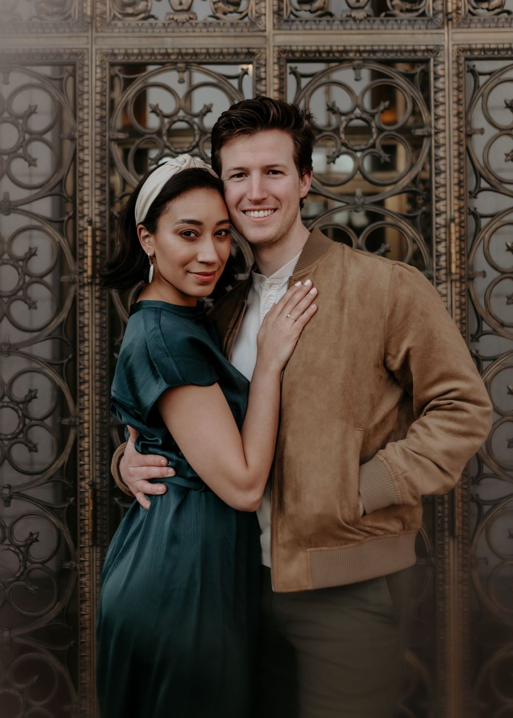 Couple poses against decorative metal gate with intricate geometric patterns.