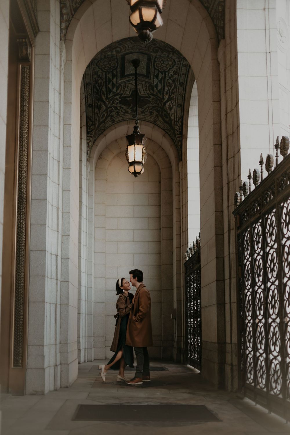 Couple shares romantic moment under ornate archway with hanging lanterns.