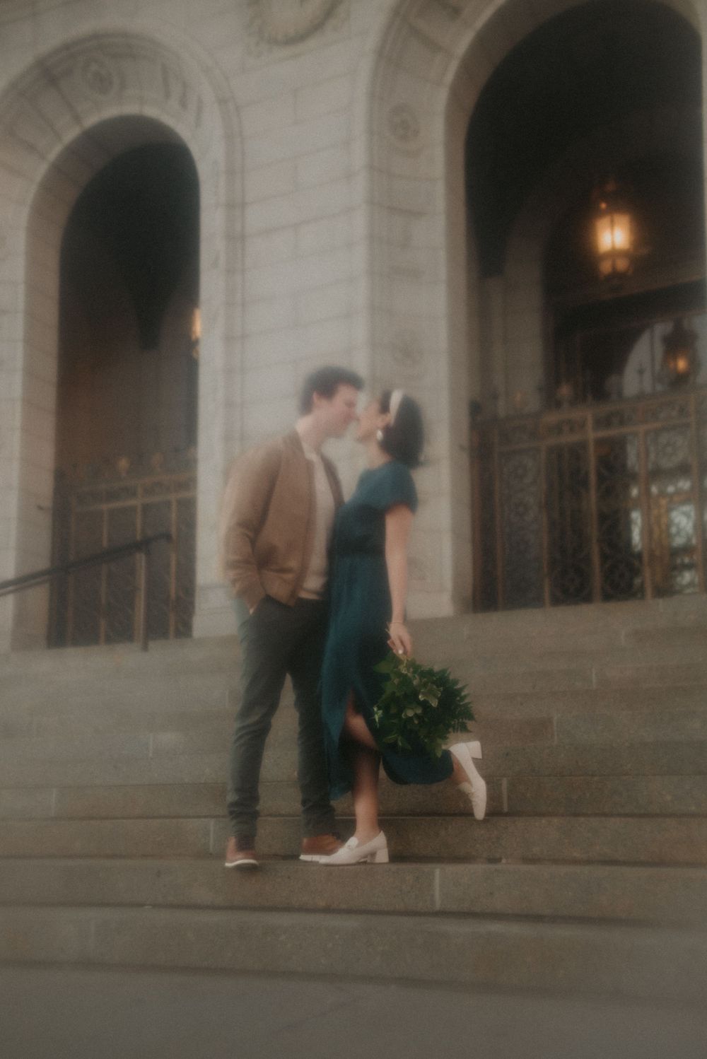 A couple shares an intimate moment on stone steps of a grand building with glowing lanterns.