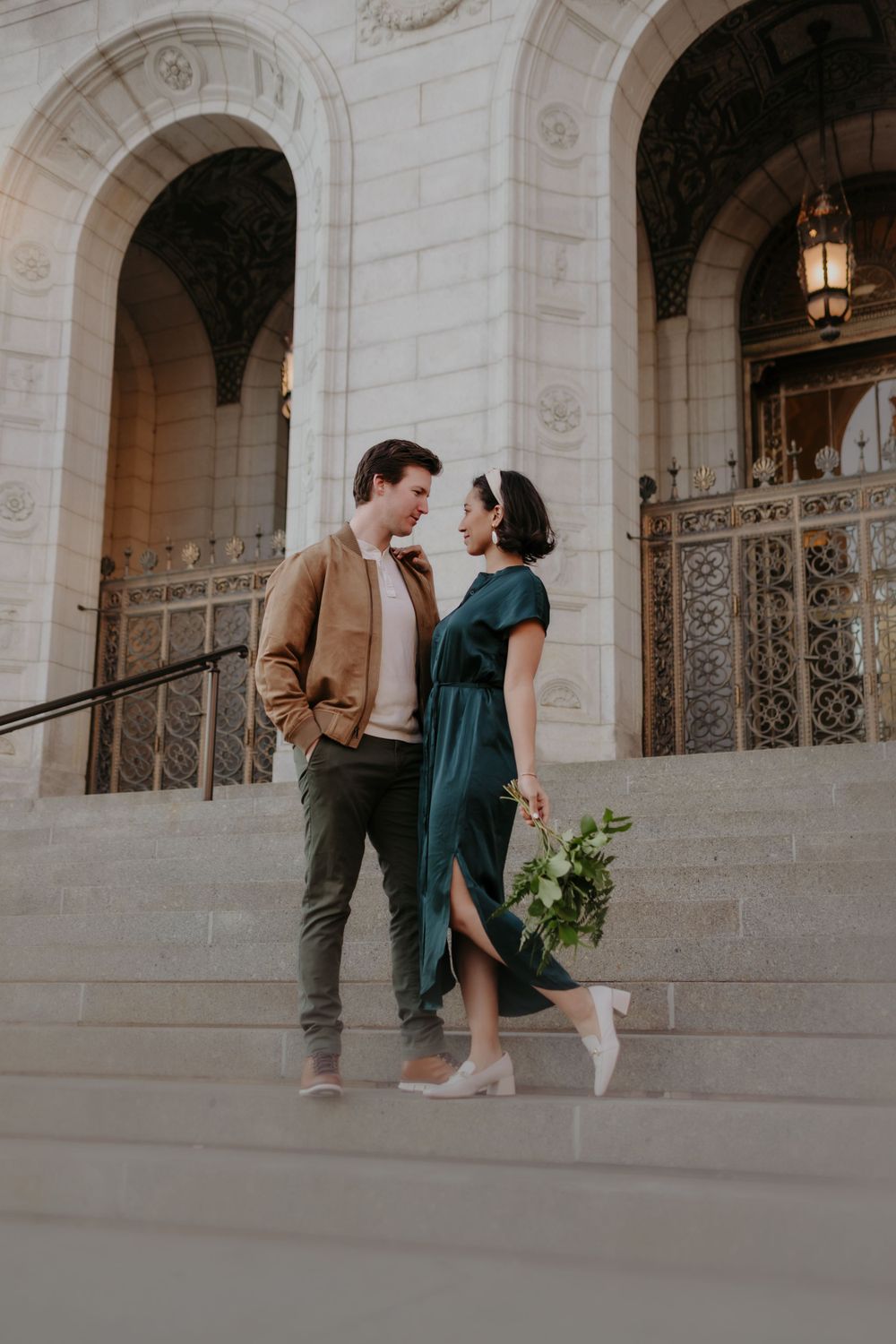 Stylish couple poses on grand stone steps with ornate architectural details.