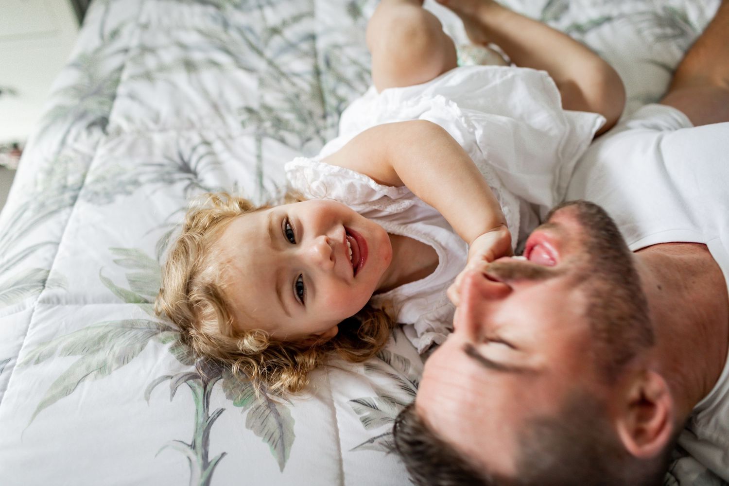 Happy child and parent share laughs while relaxing on bed with floral pattern.