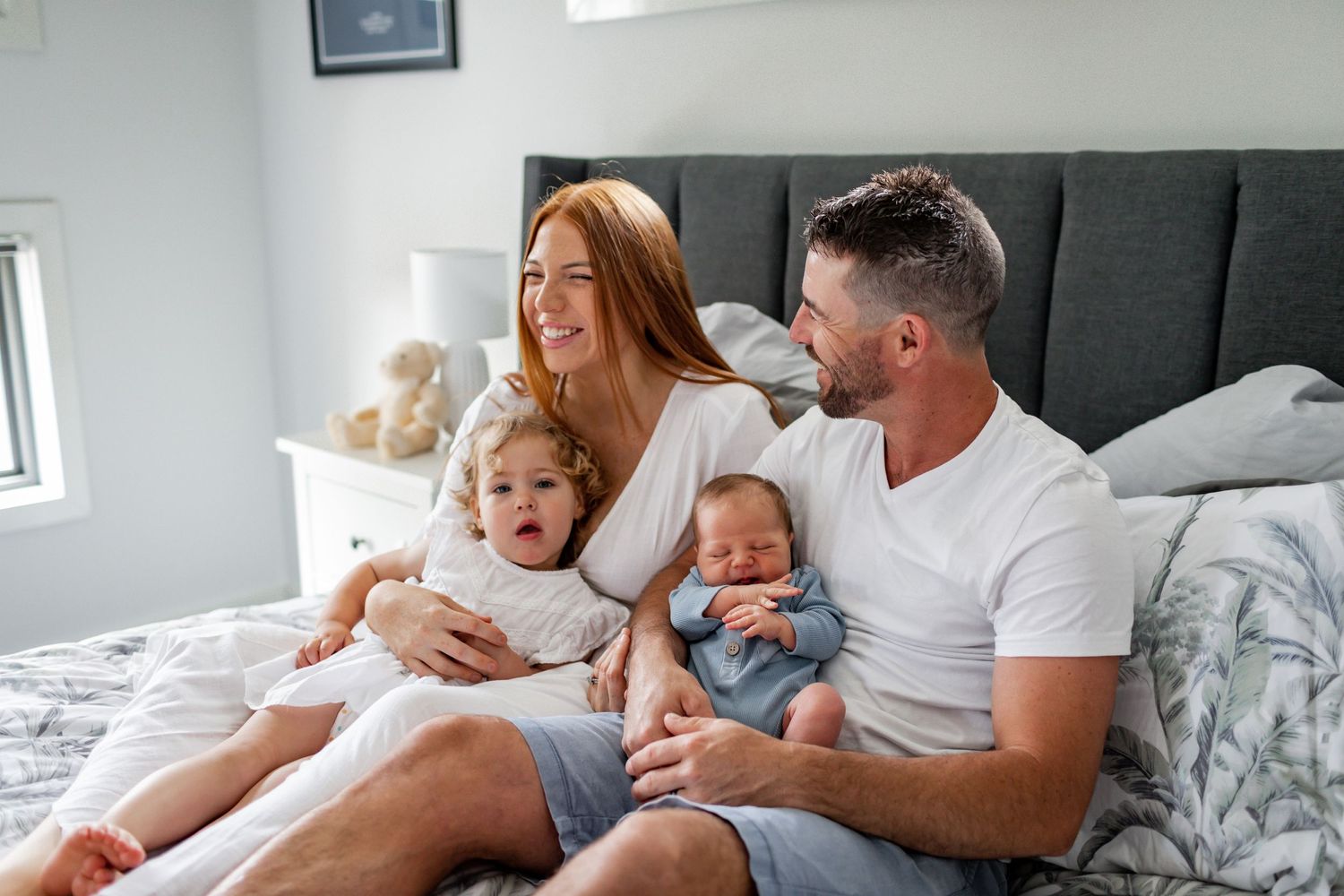 Happy family moment captured on bed with toddler and newborn siblings.