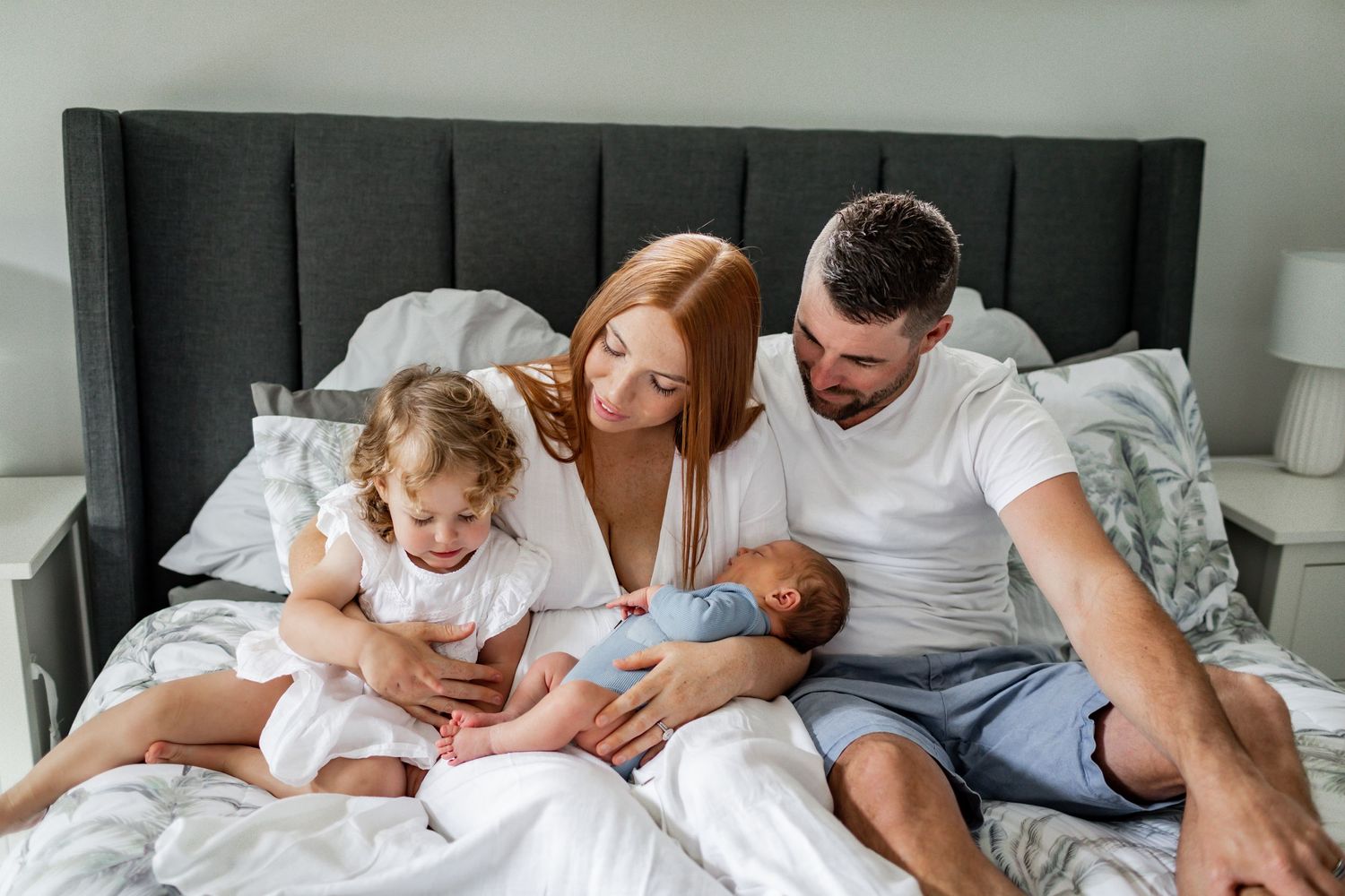 Family cuddles together on gray bedding during intimate photo session.