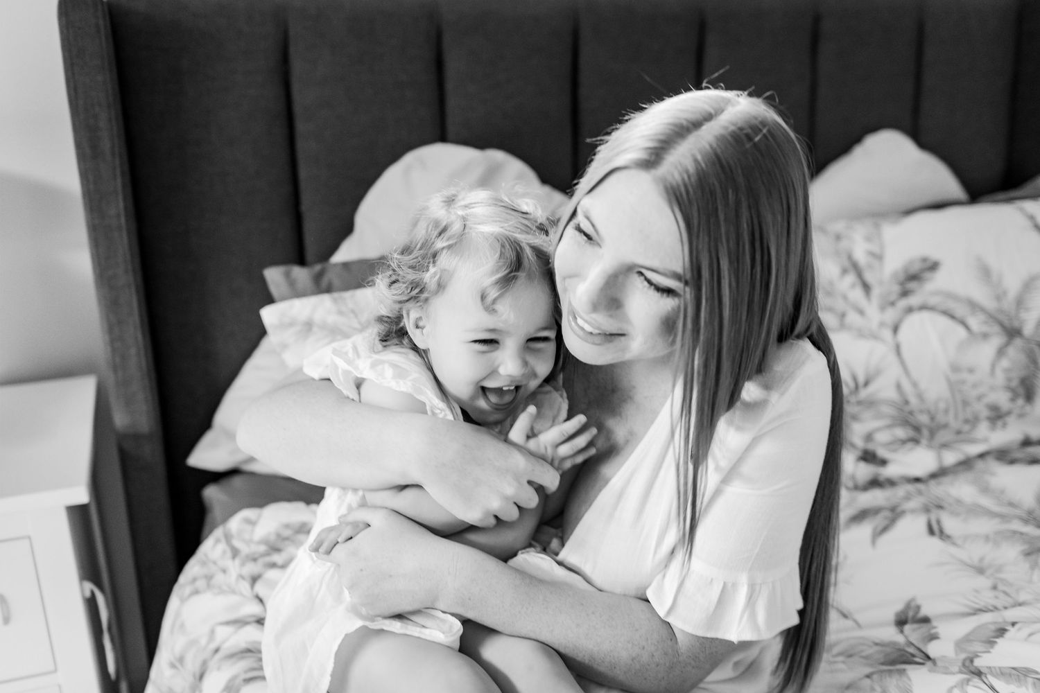 A heartwarming monochrome capture of a mother and child sharing a joyful embrace on a bed.