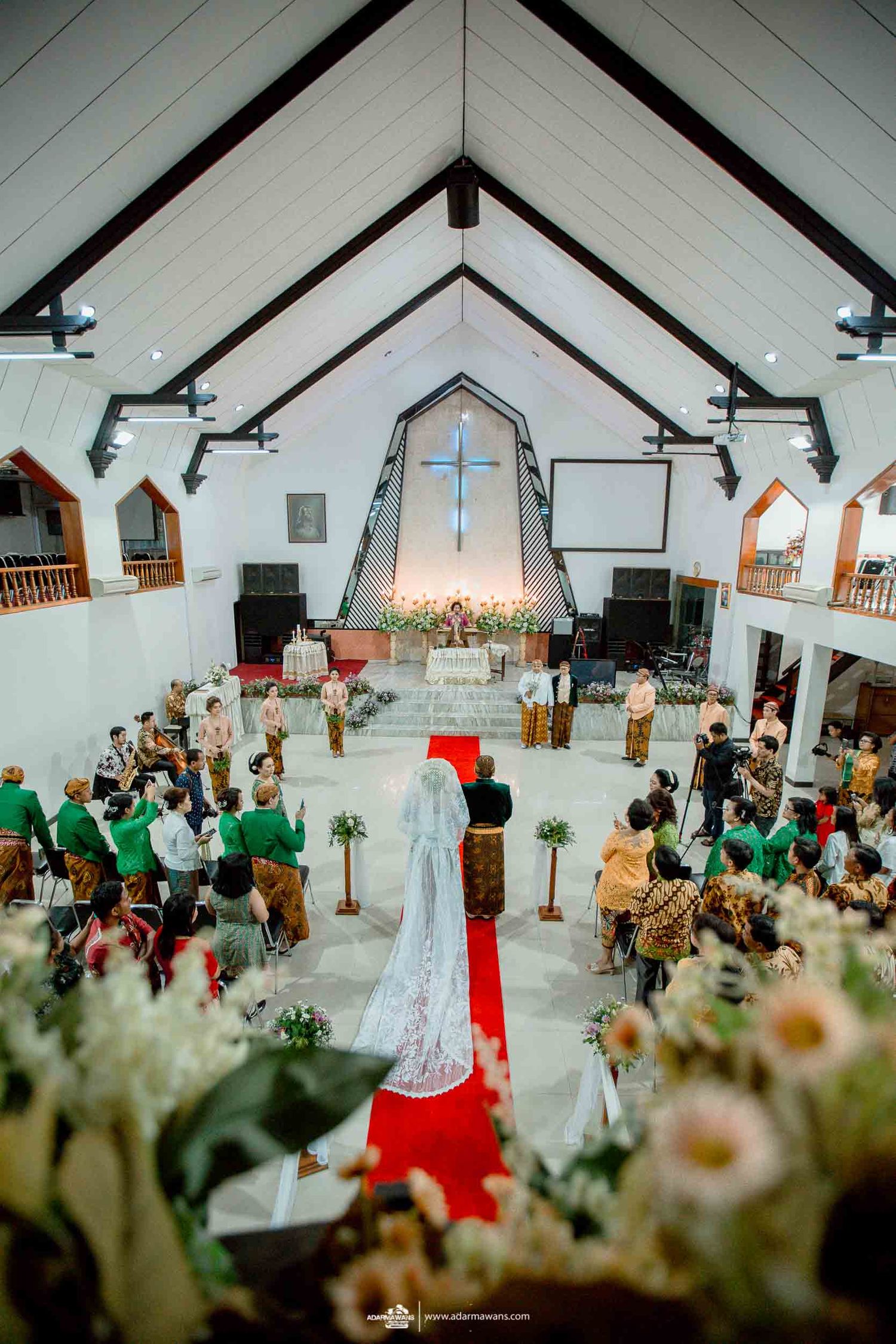 Overhead view of wedding ceremony in progress inside church with decorated altar and attendees.