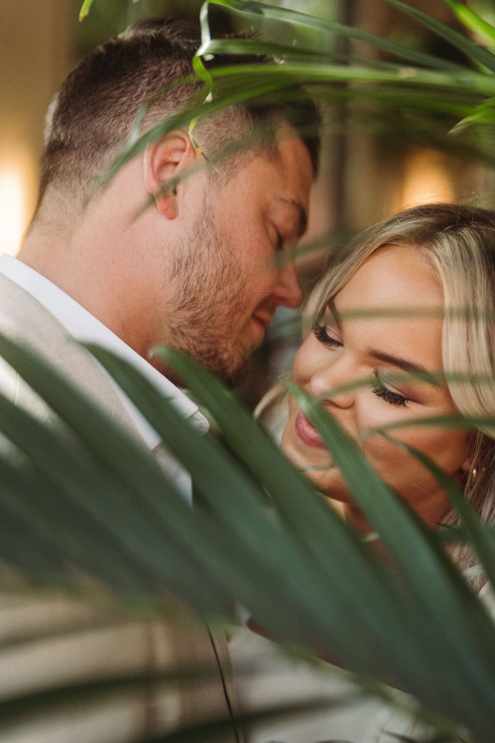 An intimate moment captured through tropical leaves in warm lighting.
