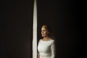 A dramatic window light illuminates a bridal portrait in a minimalist setting.