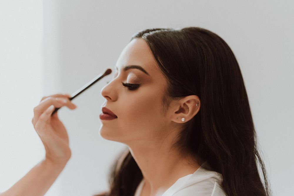 Makeup artist applies eye shadow to model with red lipstick in soft natural lighting.