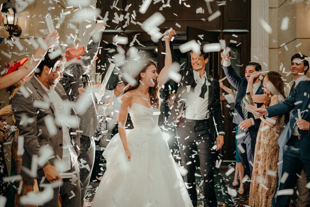 Wedding celebration with confetti shower as couple walks through crowd of cheering guests.