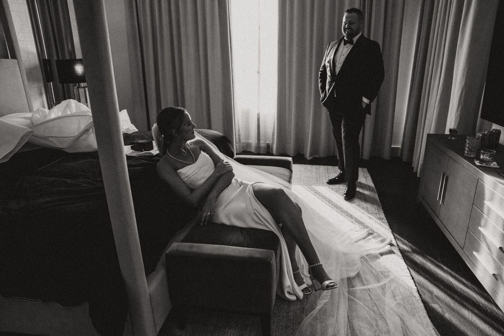 Black and white photo of wedding couple in dramatic window light in hotel room.