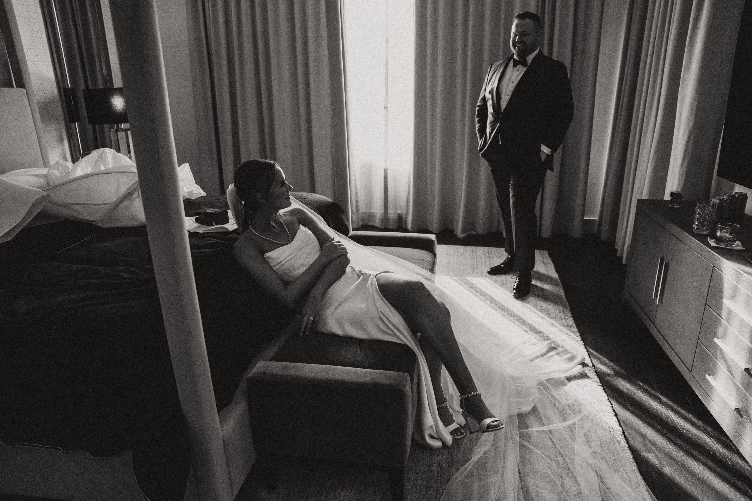 Black and white photo of wedding couple in dramatic window light in hotel room.