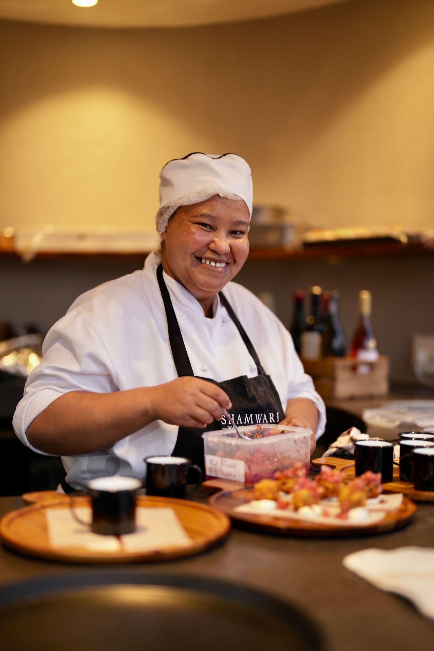 Chef preparing food in restaurant kitchen wearing white uniform and black apron.