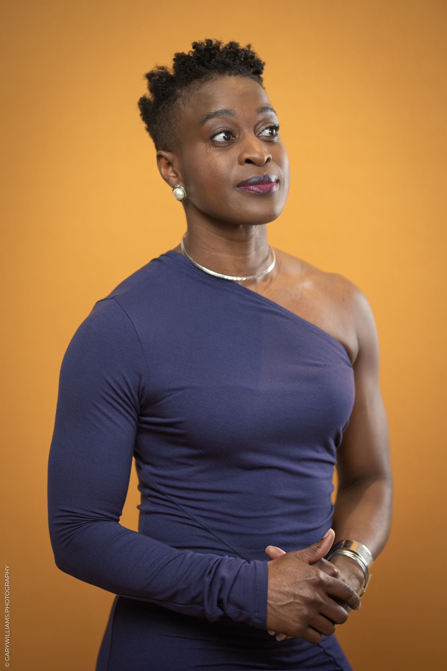 A black woman in a purple dress stands in front of a yellow wall.