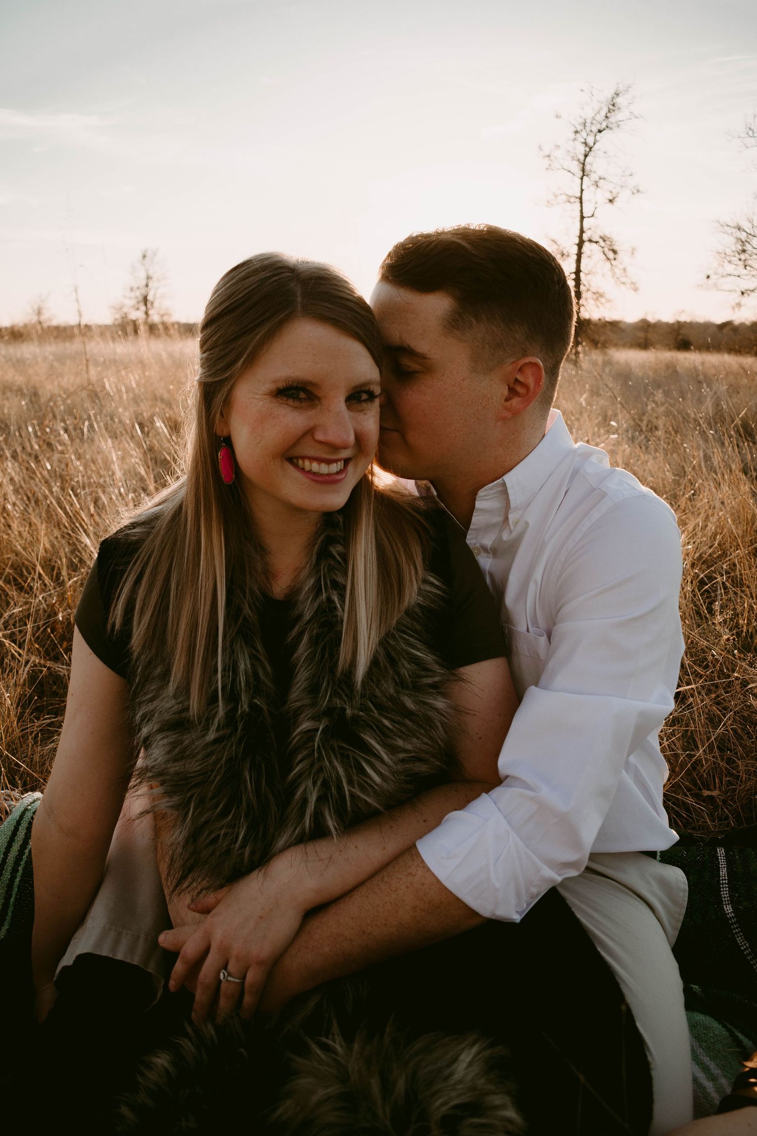 A tender moment between a couple sitting in tall grass during golden hour.