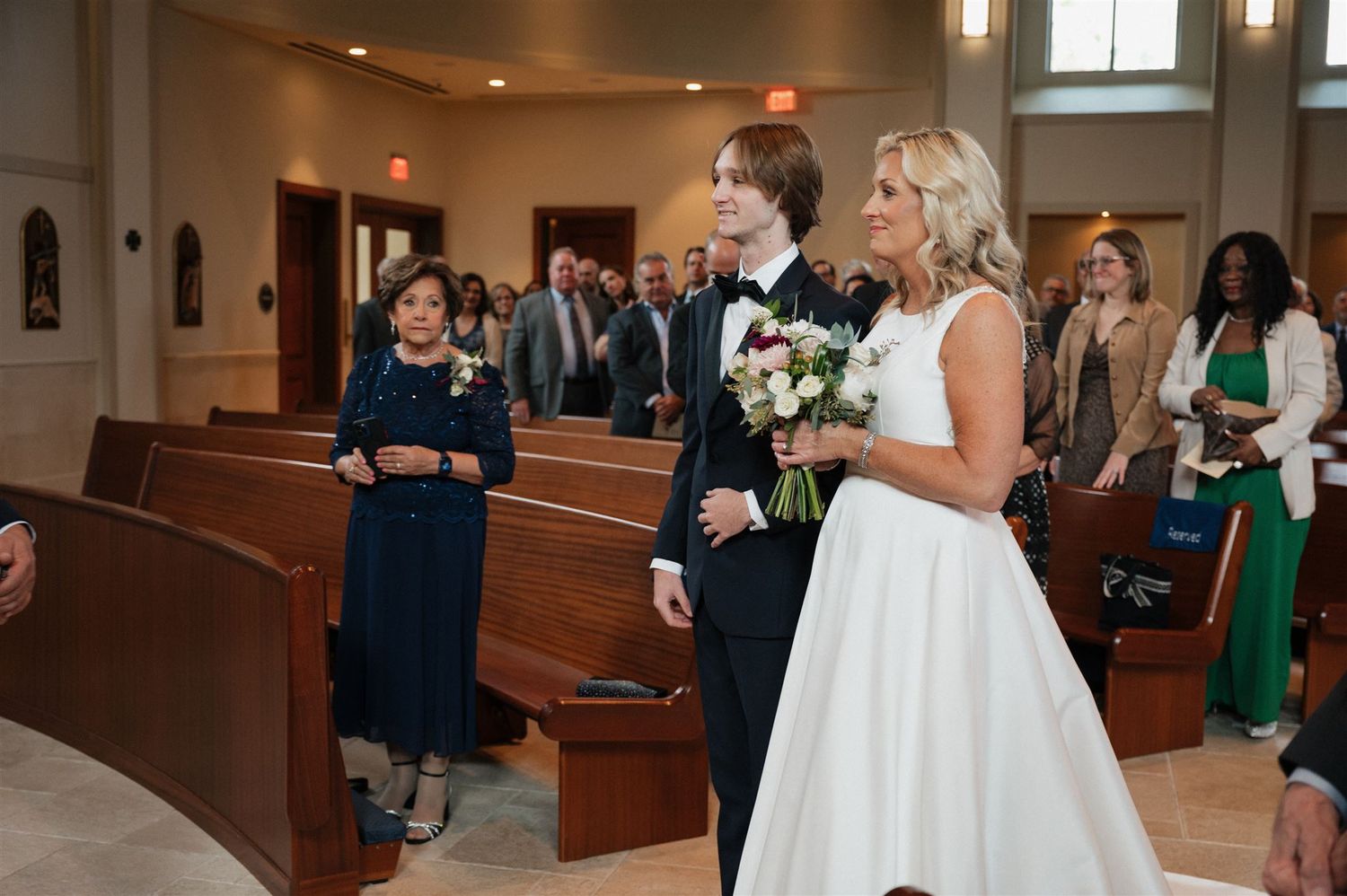 Wedding ceremony in progress with bride in white gown and guests in church pews.