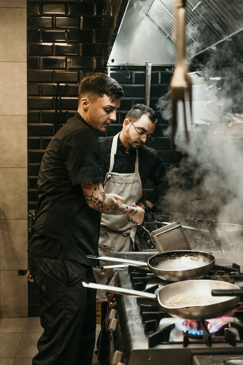 Chef working at a steaming pan in a dimly lit restaurant kitchen.