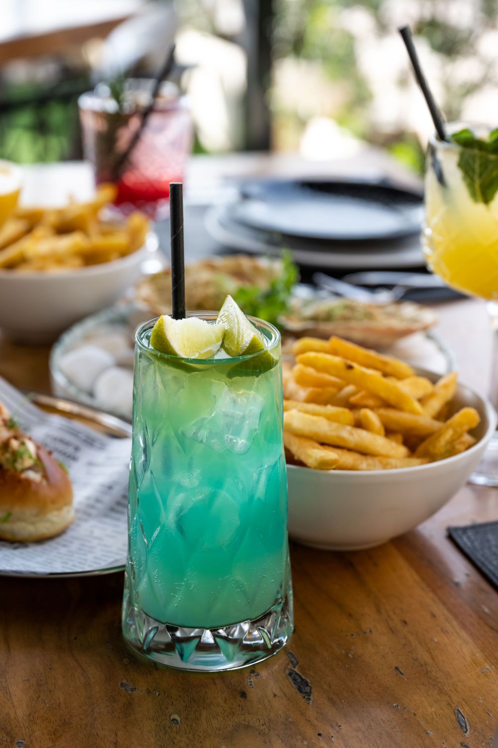 Bright blue cocktails garnished with citrus and mint served alongside french fries.
