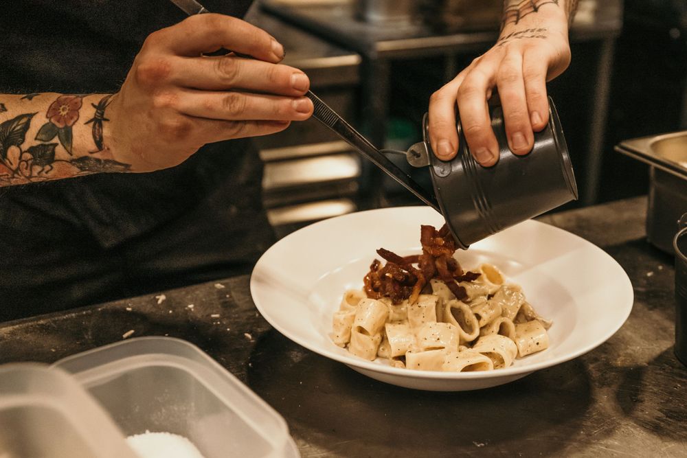 Hands preparing and plating food in a professional kitchen setting.
