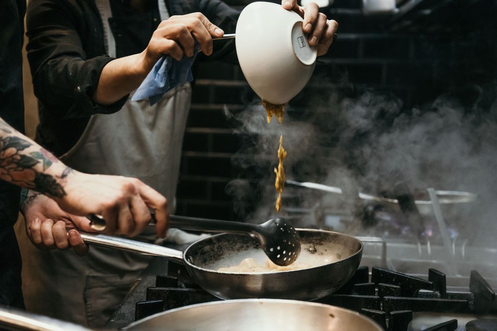 Chef cooking with steam and smoke in a dark professional kitchen environment.