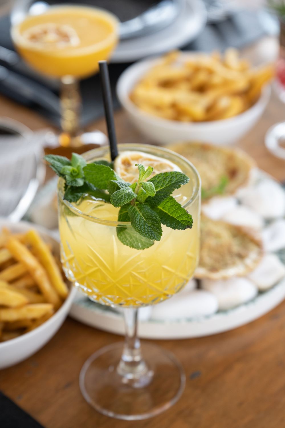 Yellow citrus cocktails garnished with fresh mint leaves on a wooden table.