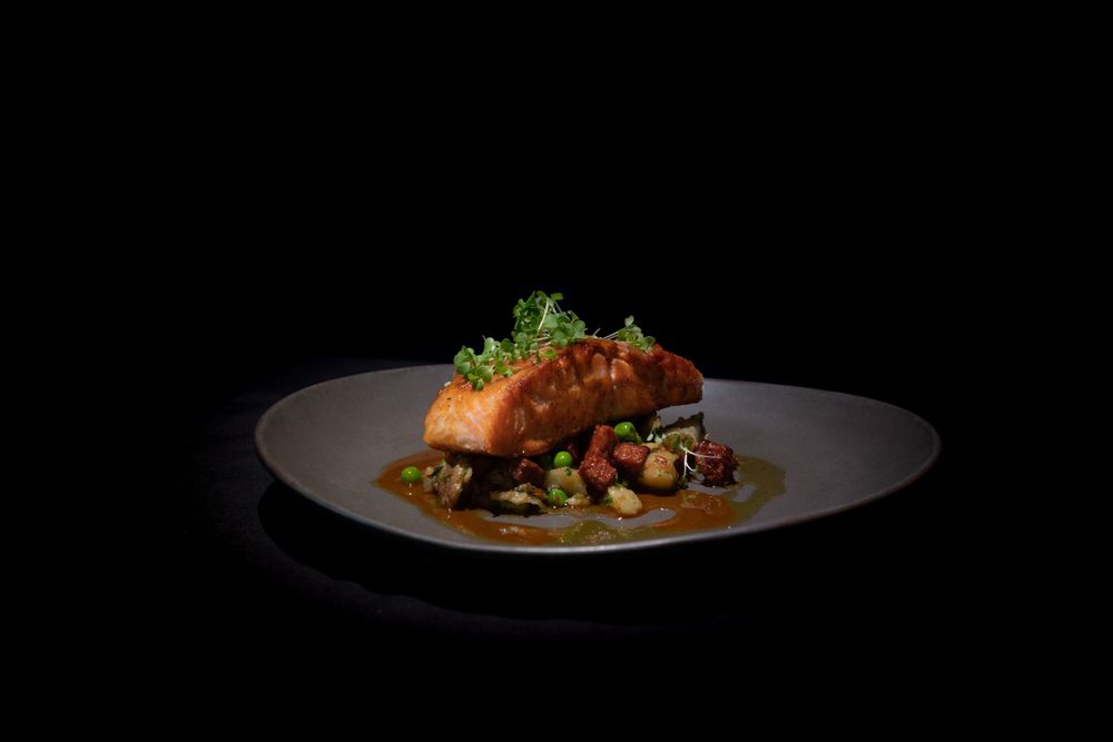 Artfully presented seafood dish with vibrant garnishes under dramatic lighting.