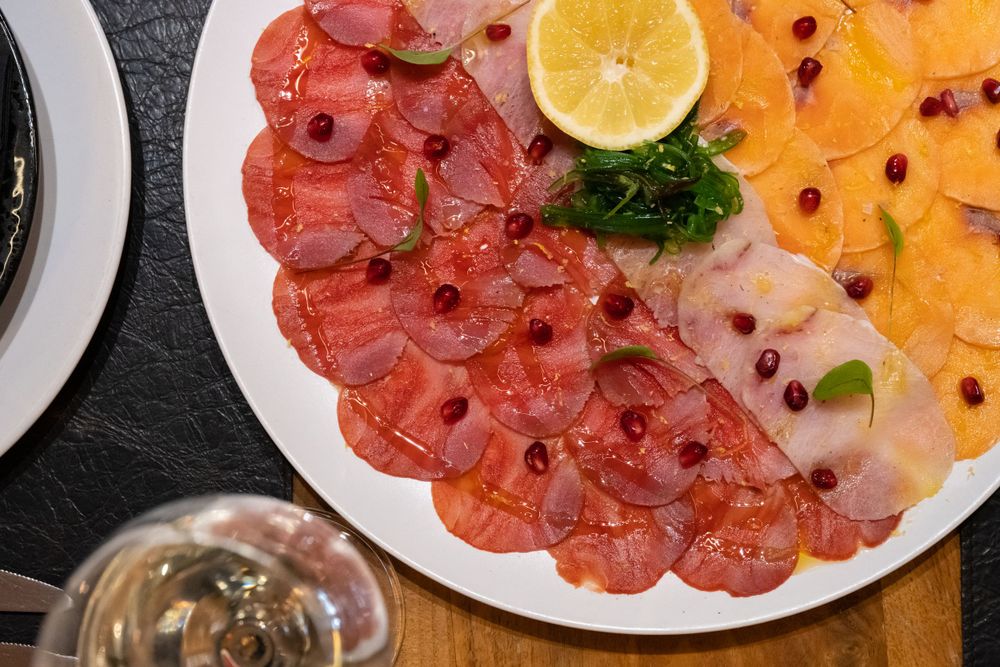 Colorful plate of salmon and tuna carpaccio garnished with citrus and herbs.