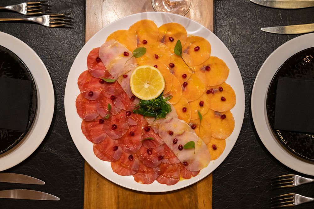 Artfully arranged seafood carpaccio with citrus and garnishes on a white plate.