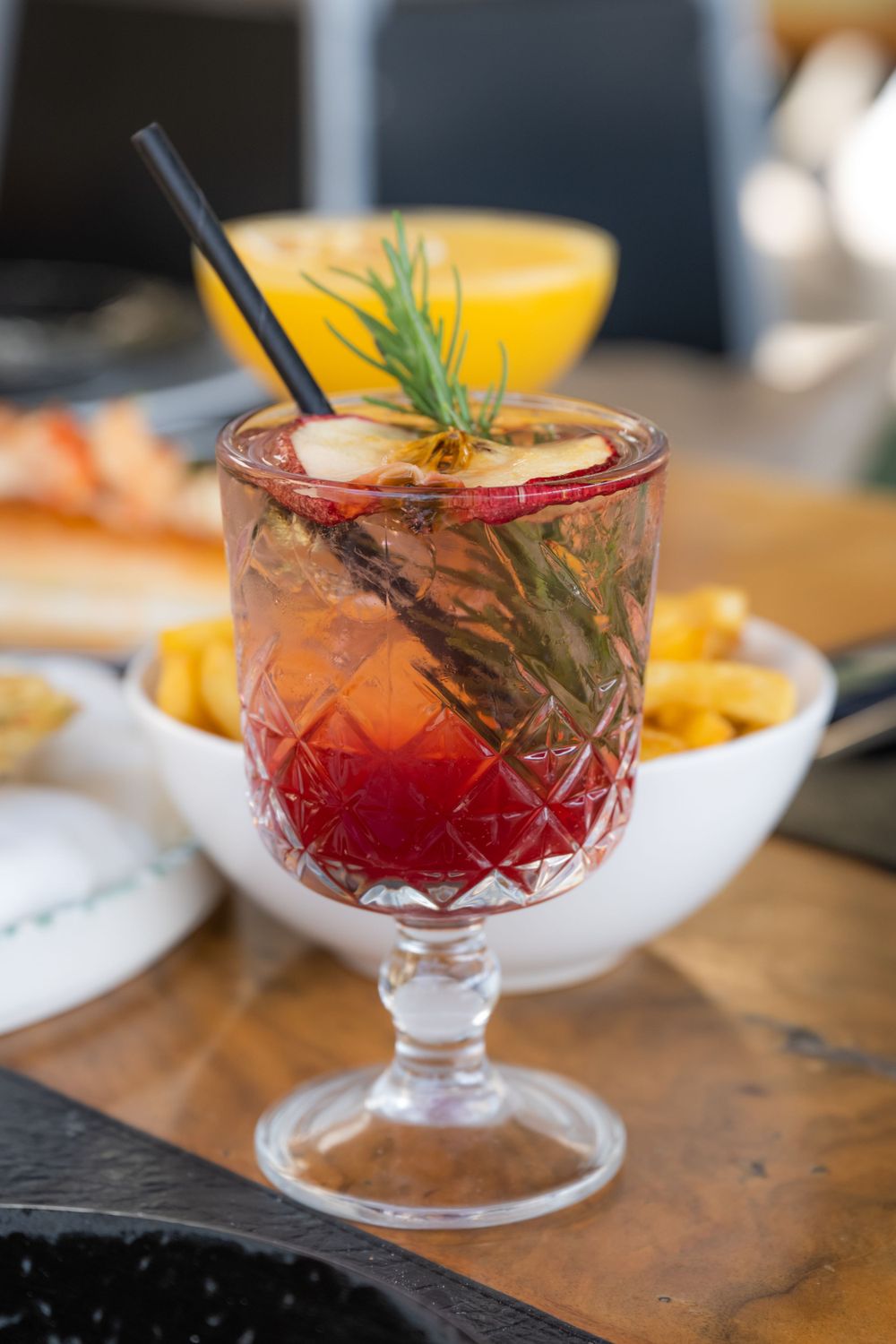 Red craft cocktails in crystal glasses garnished with herbs and citrus on a wooden surface.