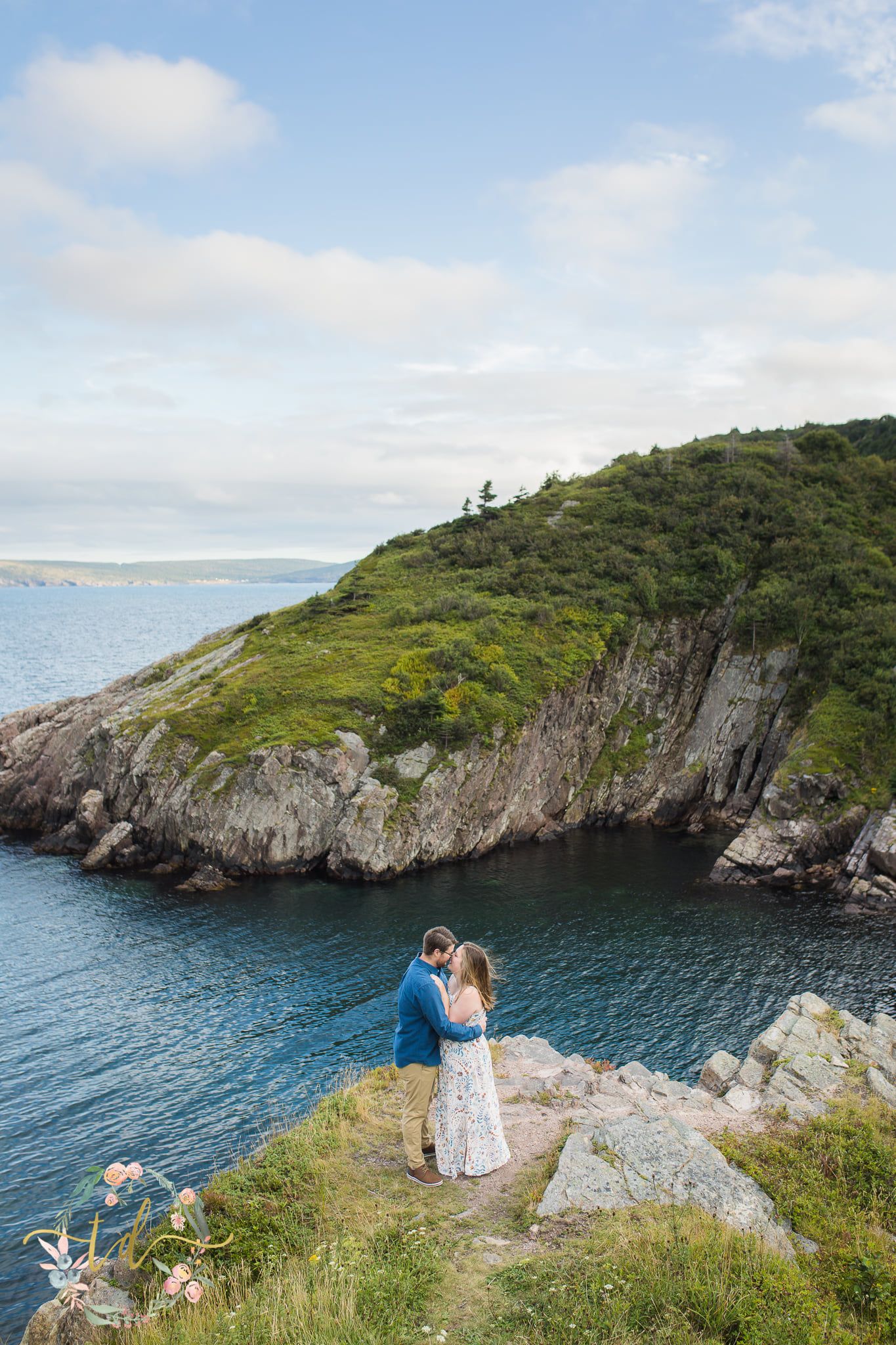 A couple stands embracing on dramatic coastal cliffs overlooking the ocean.