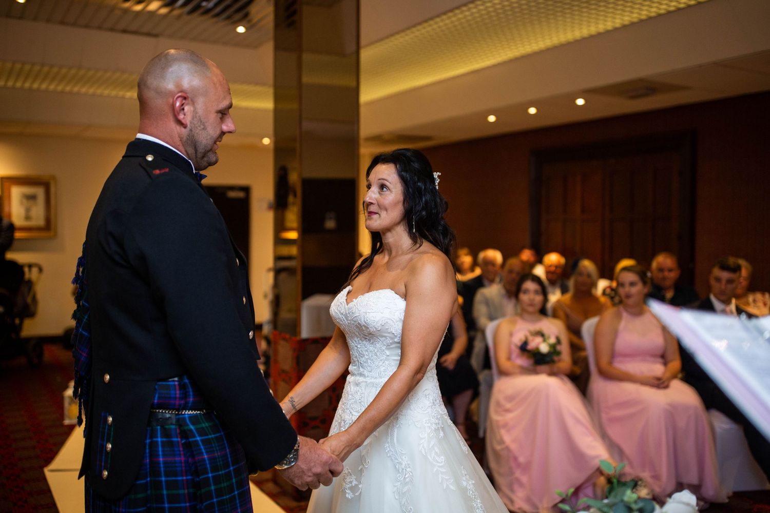 A ceremony moment in an elegant ballroom with guests watching in the background.
