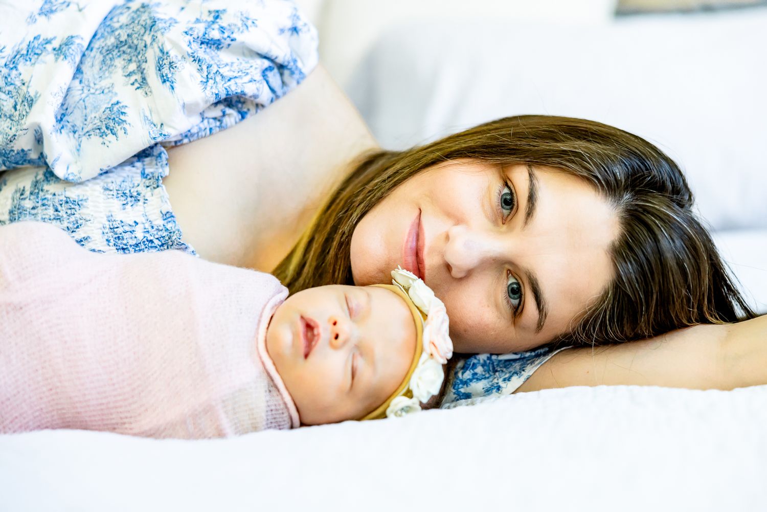 Mom lays down next to her new baby girl and smiles during lifestyle newborn photos in Colorado Springs.