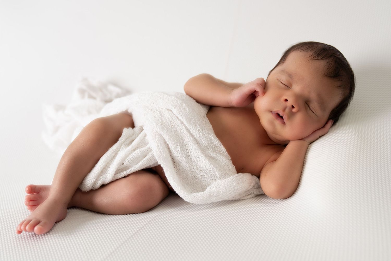 Peaceful sleeping newborn wrapped in white blanket on white background.