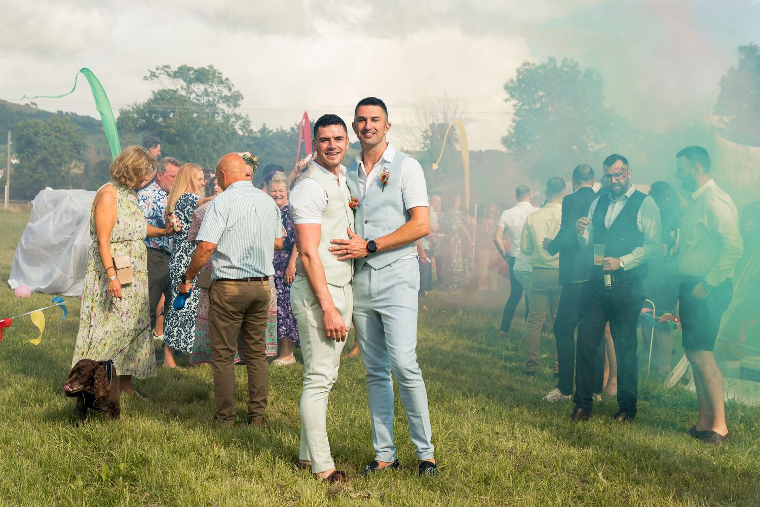 Guests celebrate with colored smoke bombs creating a festive atmosphere at an outdoor event.