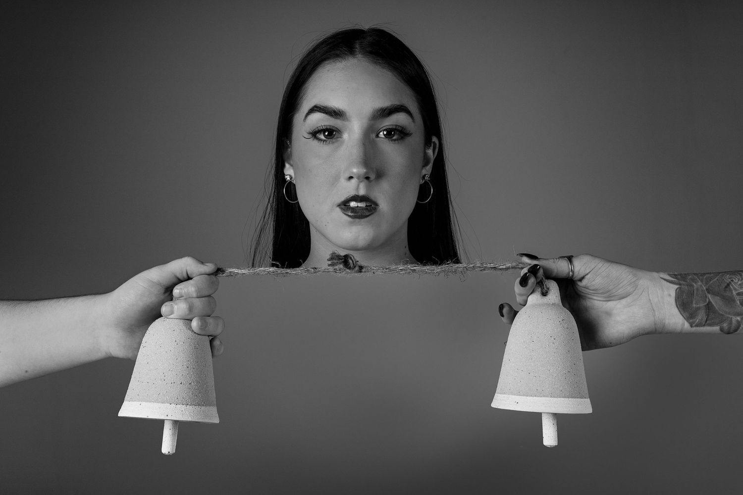 A dark artistic portrait featuring hands holding white bells on either side.