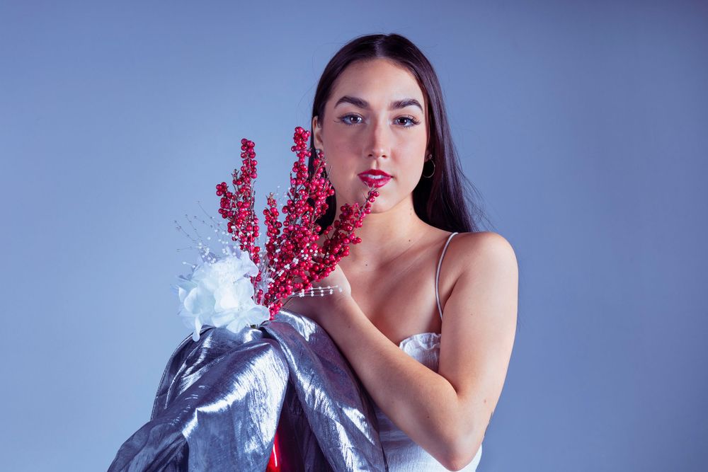 Artistic fashion photo with silver fabric and vibrant red flowers against blue background.