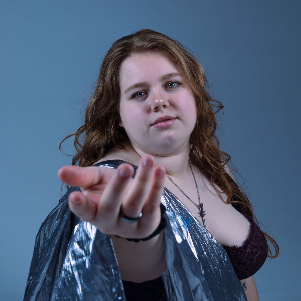 Dramatic studio portrait with metallic fabric and outstretched hand gesture.