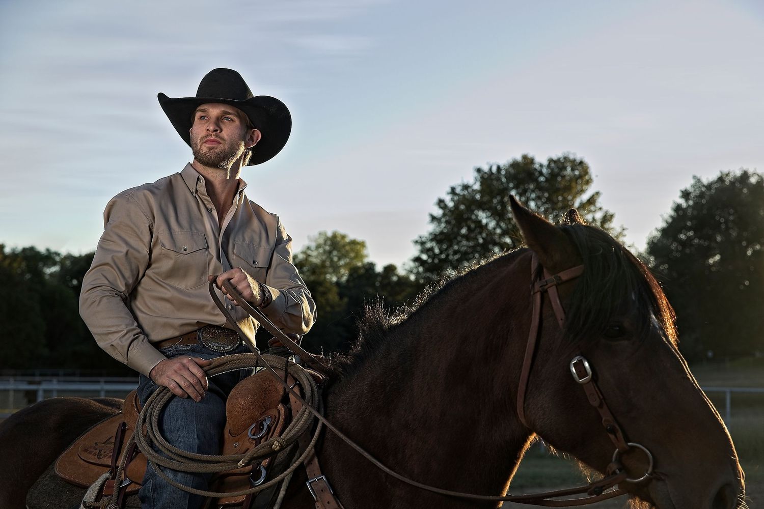 A cowboy on horseback at dusk wearing traditional Western attire and black hat.