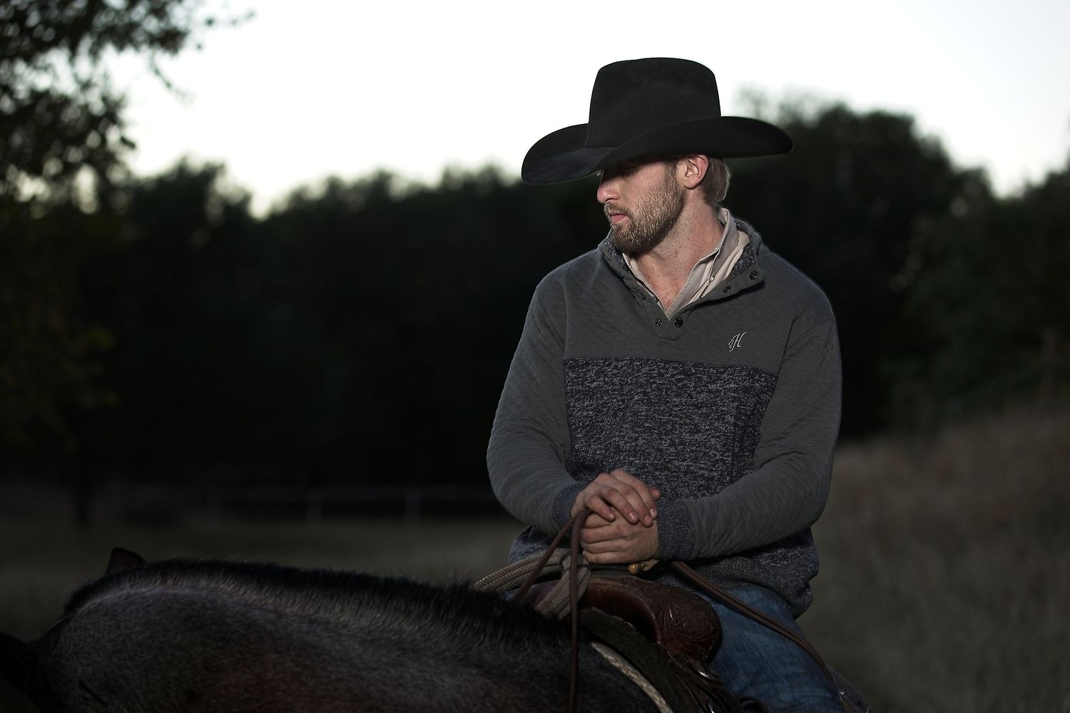 A rider in winter clothing sits mounted on horseback in low evening light.